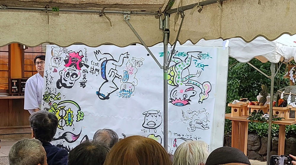 絵筆塚祭当日に参加した漫画家が大きな模造紙に描いたカッパの絵を見せるように広げている様子