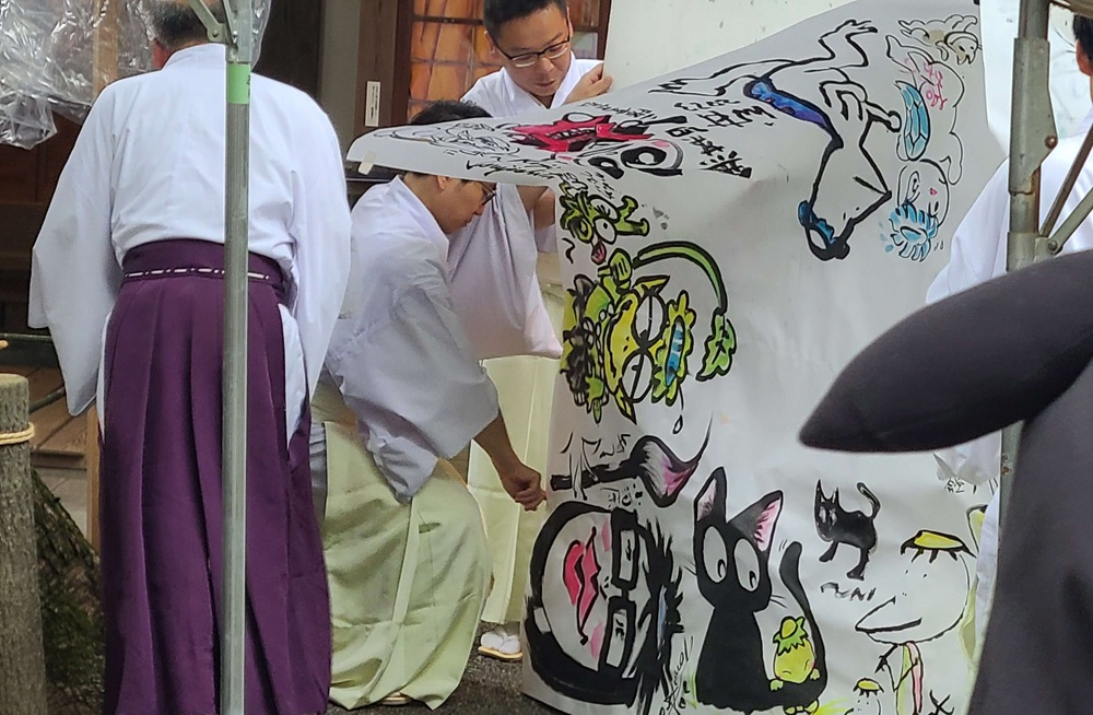 絵筆塚祭当日に参加した漫画家が大きな模造紙に描いたカッパの絵を見せるように広げ筆供養で描かれた絵をお焚き上げする様子