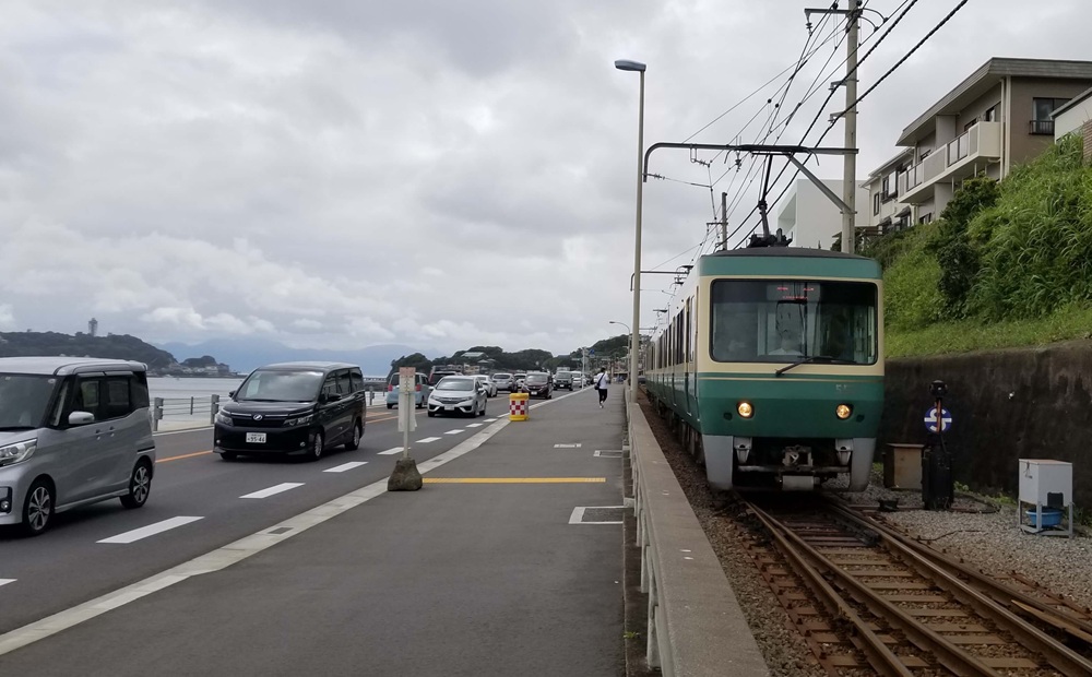 海岸沿いを走る江ノ電の様子　奥に江の島　道路には綱らる車