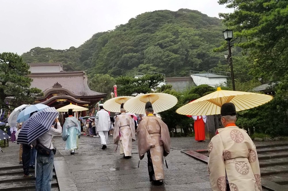 七夕祭りで舞殿に向かう神職たち 雨なので和傘を刺している